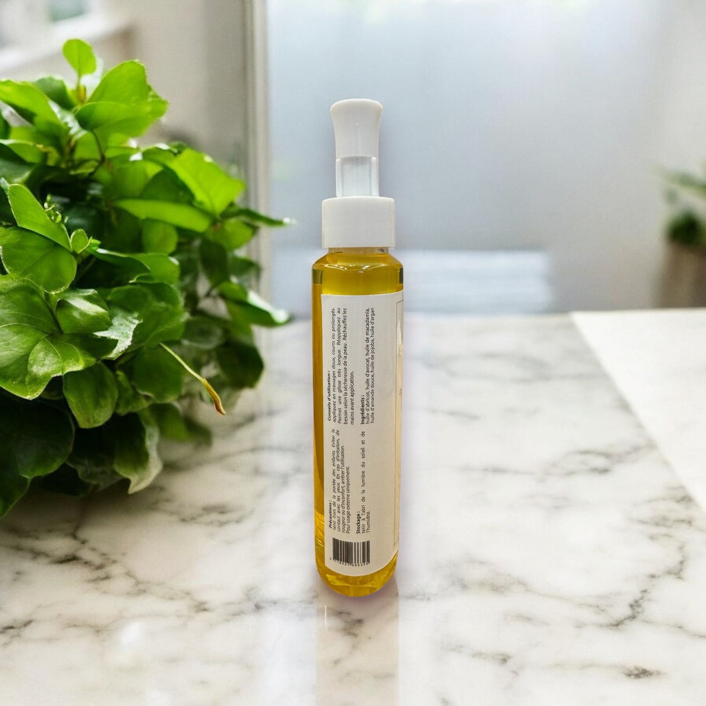 Vue arrière du flacon de l’huile de massage végétale O’Jawhar 150 ml — ingrédients et conseils d’utilisation lisibles, posé sur une surface en marbre clair avec feuillage en arrière-plan.