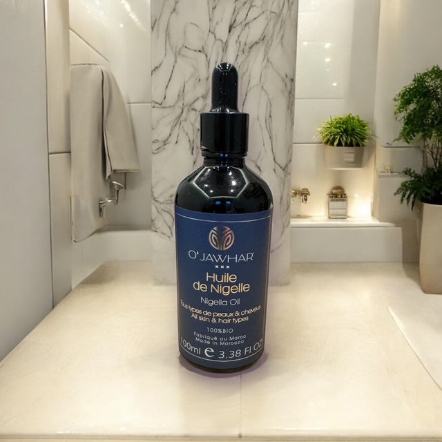 Flacon d’huile de nigelle O’Jawhar posé sur surface marbrée – soin bio pour tous types de peaux et cheveux – pressée à froid – 100 ml – certifiée ECOCERT.