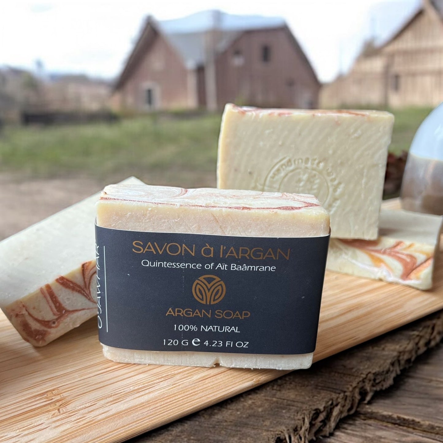 Savon à l’argan O’Jawhar mis en scène sur une planche en bois avec plusieurs savons en arrière-plan, ambiance artisanale.