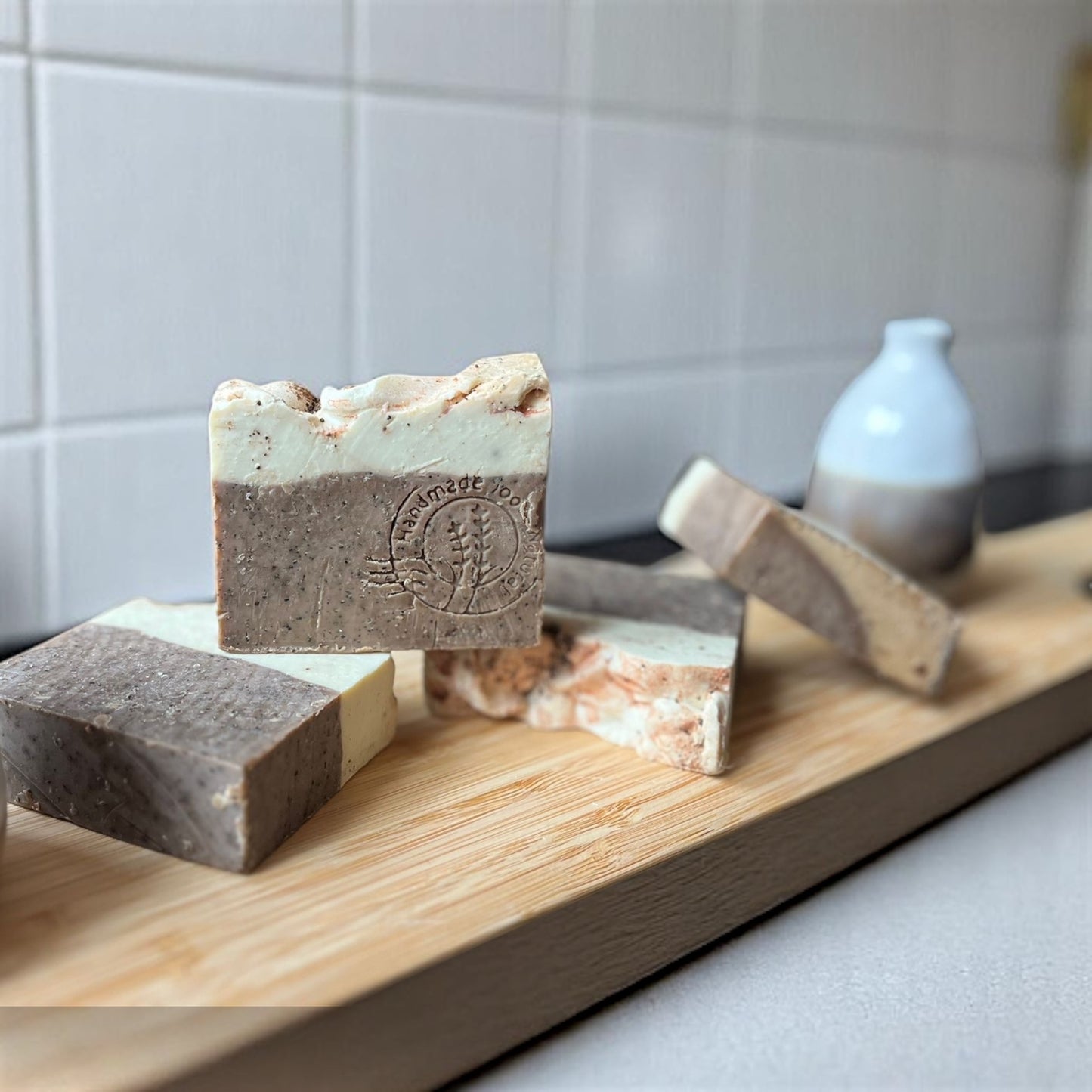 Vue rapprochée du savon au café O’Jawhar – avec son logo embossé, exposé sur une planche devant un mur carrelé blanc.