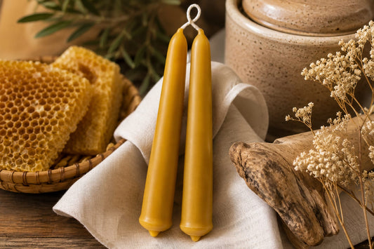 Deux chandelles artisanales en cire d’abeille naturelle d’Aït Baâmrane, présentées avec un pain de cire et un rayon de miel dans un décor chaleureux.